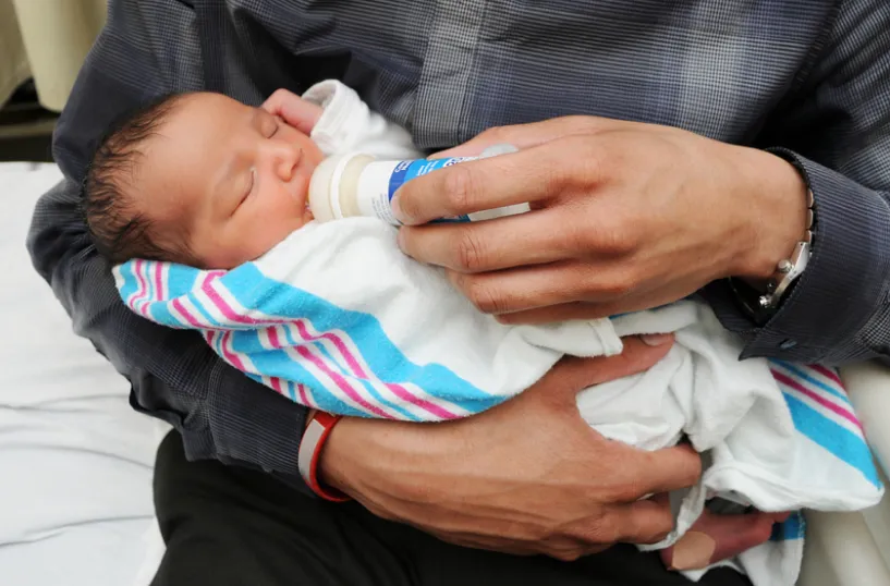 A man is feeding a baby from a formula bottle.